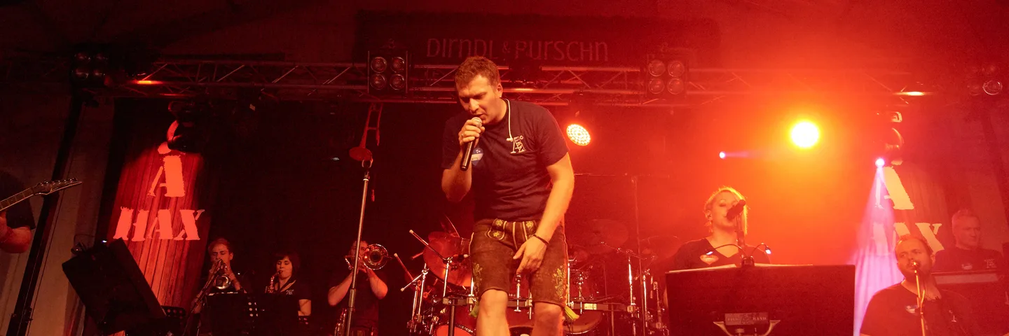 Die Band Ä-Hax spielt im rot beleuchteten Festzelt, vorne der Sänger in Lederhose am Mikrofon