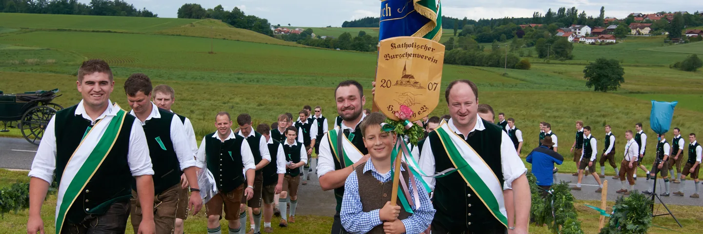 Der Verein zieht in Tracht mit grüner Fahne durch Halsbach zum Burschenfest