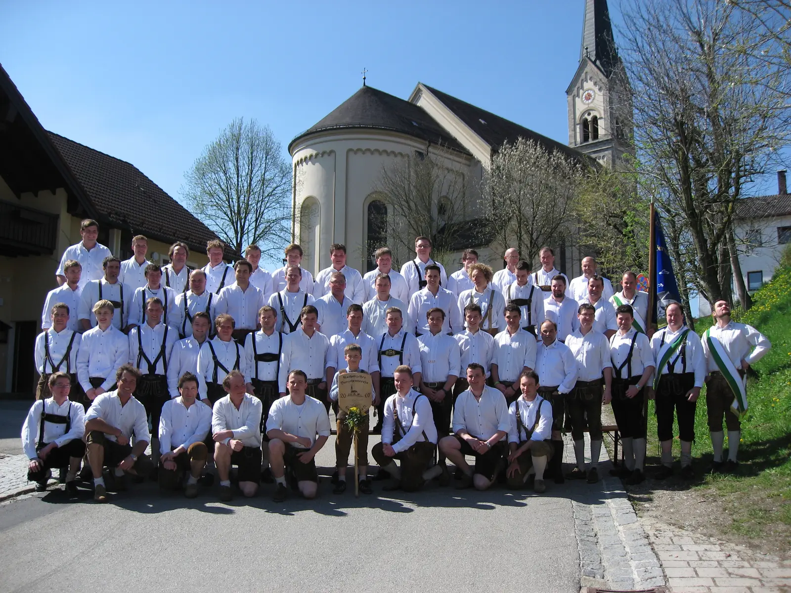 Rund fünfzig Burschen in weißem Hemd und Lederhose stehen vor der Pfarrkirche, rechts am Rand die neue blaue Vereinsfahne.