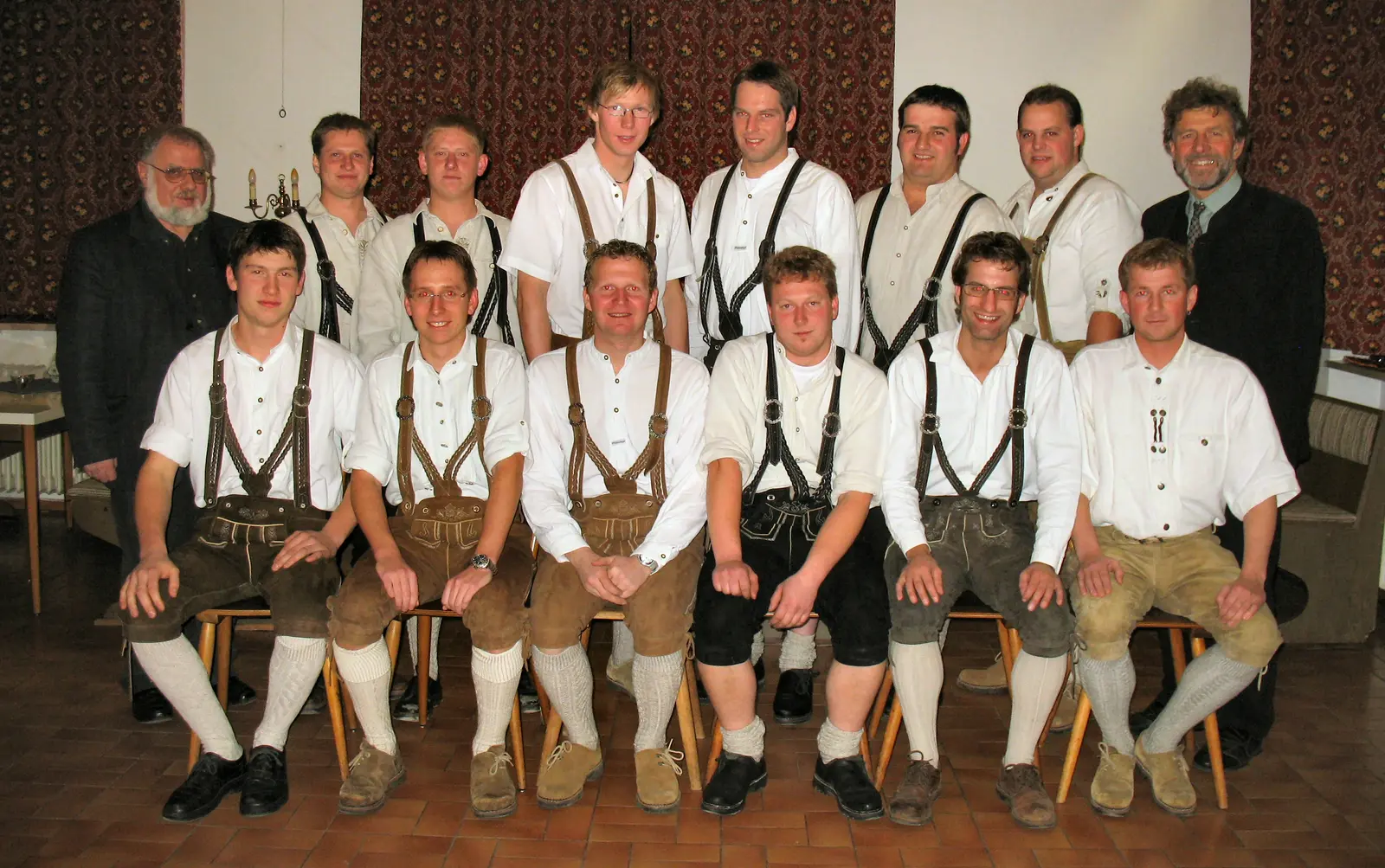 Gruppenbild der Gründungsmitglieder beim Mitterwirt: vorne sechs Burschen auf Stühlen, dahinter stehend weitere in weißem Hemd und Lederhose, außen zwei Männer im Anzug.