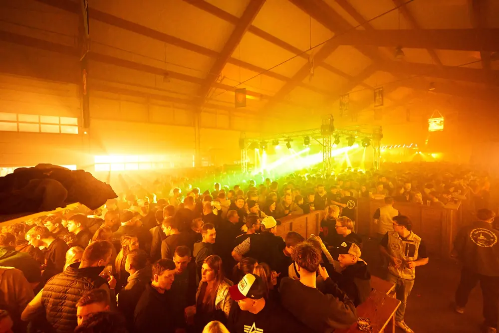 Volle Halle mit Nebel, warmem Licht und grünen Laserstrahlen über der Menge
