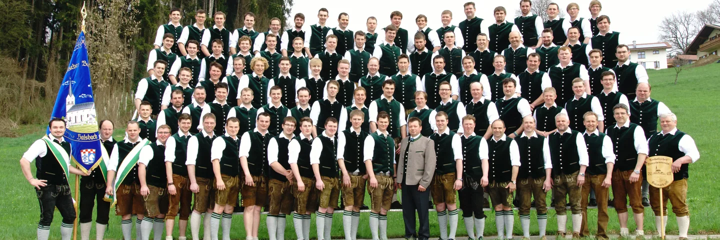 Die Burschen in grünen Westen und Lederhosen stehen in Reihen zum Vereinsfoto, links die Vereinsfahne