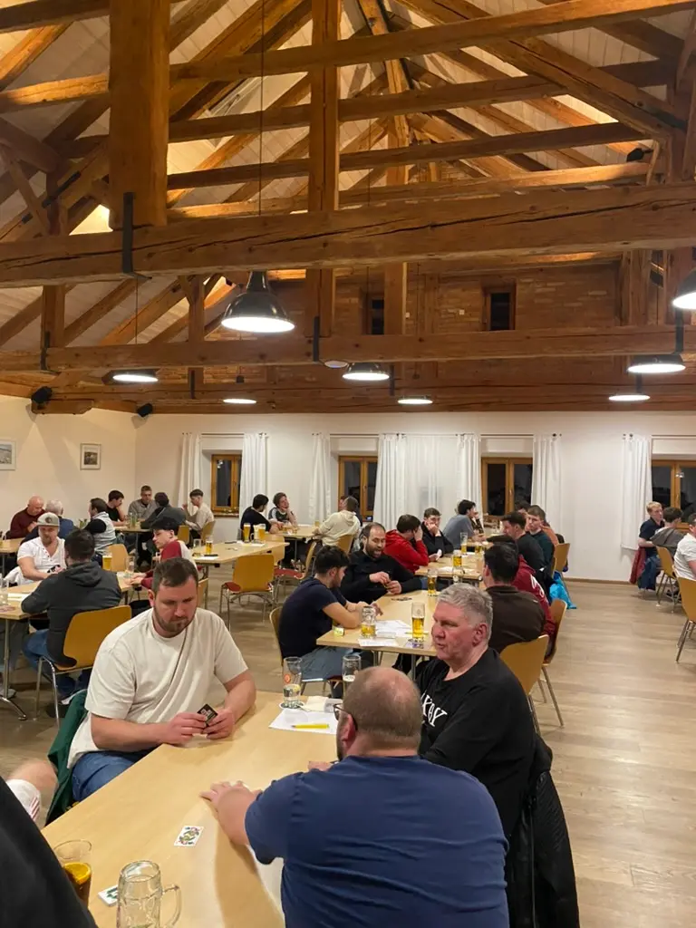 Volle Tischreihen unter offenem Holzdachstuhl beim Wattturnier, Karten und Bierkrüge auf den Tischen